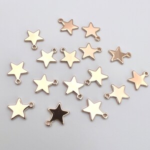 K&ouml;nnte beinhalten: Eine Sammlung von 16 goldfarbenen sternf&ouml;rmigen Charms mit einem Sprungring. Jeder Charm hat ein f&uuml;nfzackiges Sternendesign mit einer Schlaufe oben.