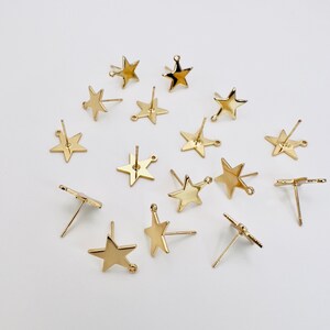May include: A collection of gold-colored star-shaped earring posts. The earrings have a simple, minimalist design, with a post for insertion into the ear and a small loop for attaching charms. The earrings are scattered on a white surface.