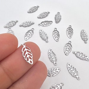 May include: A collection of silver metal leaf charms with a delicate cutout design. The charms are scattered on a white surface.