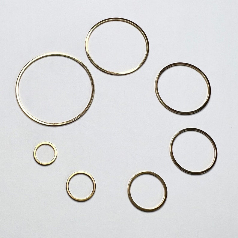 May include: A set of seven gold-coloured metal hoops of varying sizes. The hoops are arranged in a circle on a white background.