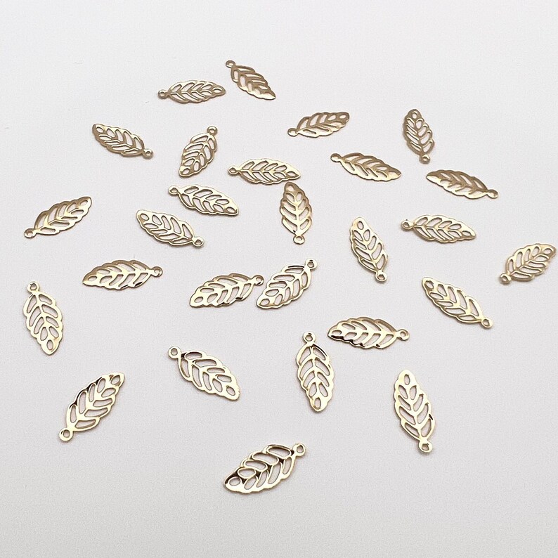May include: A collection of gold-colored metal leaf charms. The charms are delicate and intricate, with a cutout design. They are perfect for adding a touch of elegance to jewelry or crafts.