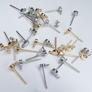 K&ouml;nnte beinhalten: Eine Sammlung von silbernen und goldenen Ohrring-Stiften mit verschiedenen Arten von Ohrring-R&uuml;cken. Die Ohrring-Stifte sind alle etwa 2,5 cm lang.