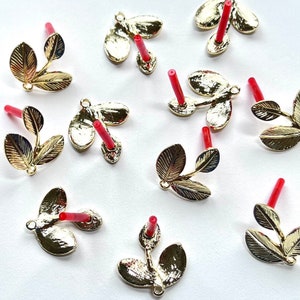 May include: Ten gold leaf charms with red stems. Each charm features three leaves and a loop for attaching to a jewelry piece.