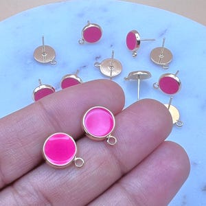 May include: A close-up of ten gold-toned earring posts with pink round cabochons. The earring posts have a loop on the back for attaching a charm or dangle.
