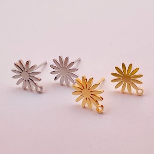 May include: Four daisy-shaped stud earrings in silver and gold tones. Each earring features a central disc surrounded by petals. Two are silver, and two are gold, with a small loop for attaching to other jewelry.
