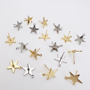 May include: A collection of star-shaped stud earrings in gold and silver tones. The earrings have a post and a small loop for attaching to a backing. The stars are arranged on a white surface.