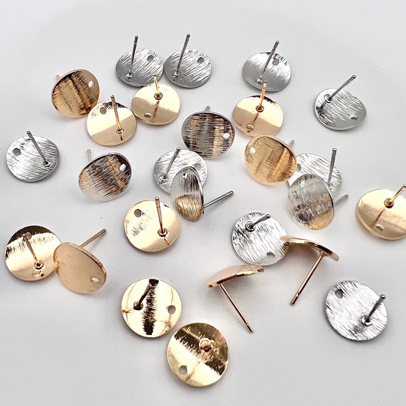 May include: A collection of round earring blanks in gold and silver tones. The blanks are made of metal and have a textured finish. They are perfect for creating custom earrings.