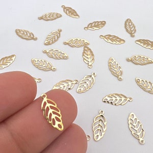 May include: A collection of gold-colored metal leaf charms with a delicate, intricate design. The charms have a hole at the top for attaching to jewelry or other crafts.