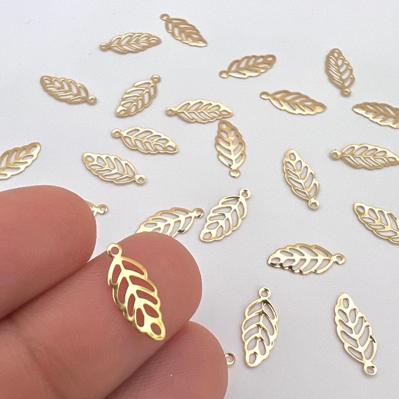 May include: A collection of gold-colored metal leaf charms with a delicate, intricate design. The charms have a hole at the top for attaching to jewelry or other crafts.