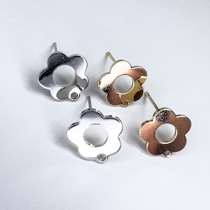 May include: Three silver flower-shaped earring posts. The earrings are in the shape of a simple flower with a hole in the center. The earrings are on a white background.