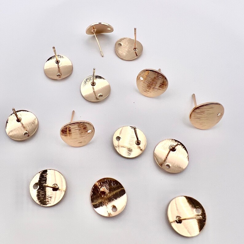 May include: A set of 11 gold-toned earring blanks. Each blank is a round disc with a small hole in the center. The blanks are designed for use with earring posts.