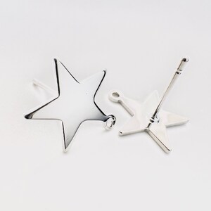 May include: Two silver star-shaped stud earrings. The earrings have a polished, reflective surface and a simple, minimalist design. The star studs are on a white background, showcasing their bright, metallic appearance. The earrings are a jewelry item.