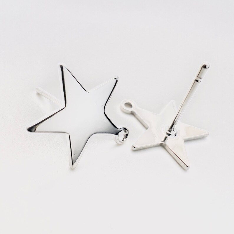 May include: Two silver star-shaped stud earrings. The earrings have a polished, reflective surface and a simple, minimalist design. The star studs are on a white background, showcasing their bright, metallic appearance. The earrings are a jewelry item.