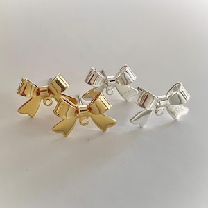 May include: Four bow-shaped stud earrings. Two are gold-colored, and two are silver-colored. The earrings have a post and a small loop at the bottom of the bow.