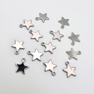 K&ouml;nnte beinhalten: Eine Sammlung von 14 silbernen sternf&ouml;rmigen Charms mit einer Schlaufe an jeder Seite. Die Charms sind auf einer wei&szlig;en Oberfl&auml;che angeordnet.