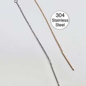 May include: Two threader earrings, one silver-colored and one gold-colored, are displayed against a white background. Each earring features a delicate chain and a straight bar at the end. The text "304 Stainless Steel" is in a white circle.