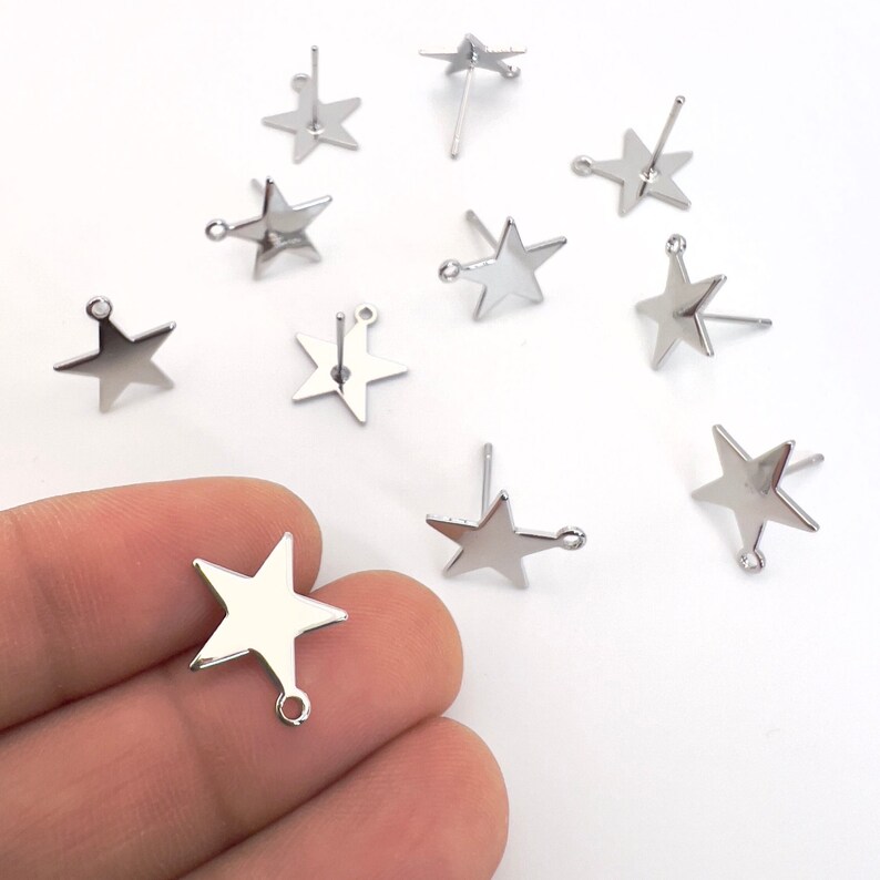 May include: A collection of shiny, silver-colored star-shaped earring components. Each star has a post for piercing and a small loop at the bottom. The earrings are displayed on a white surface.