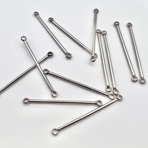 May include: A collection of silver-colored, straight bar jewelry findings with a small loop at each end. These findings are scattered on a white surface, and are suitable for jewelry making.