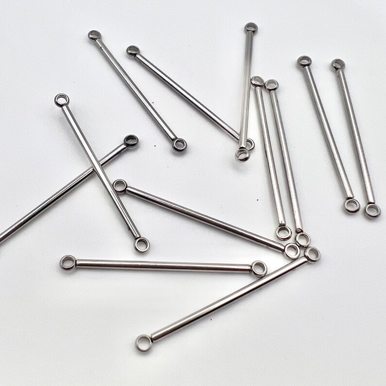 May include: A collection of silver-colored, straight bar jewelry findings with a small loop at each end. These findings are scattered on a white surface, and are suitable for jewelry making.