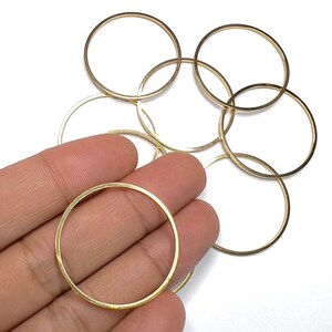 May include: A set of six gold-coloured metal jump rings. The rings are all the same size and are arranged in a pile.