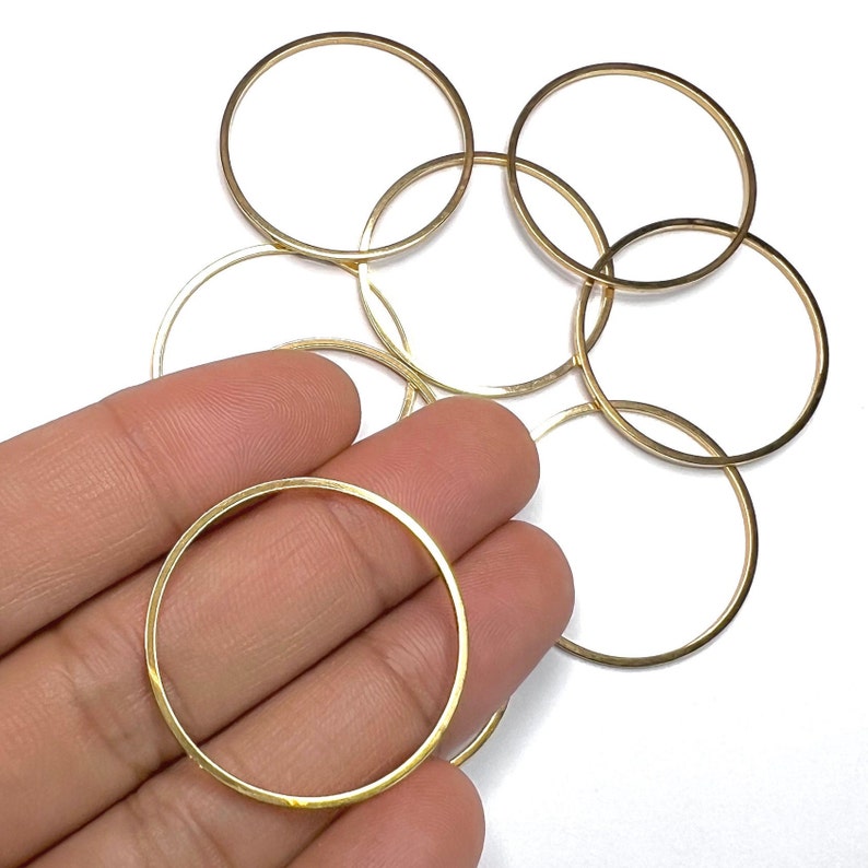 May include: A set of six gold-coloured metal jump rings. The rings are all the same size and are arranged in a pile.