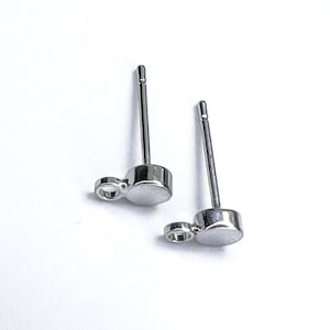 K&ouml;nnte beinhalten: Ein Paar silberne Ohrstecker mit einem kleinen Kreis-Anh&auml;nger, der an jedem Ohrstecker h&auml;ngt. Die Ohrringe haben ein schlichtes, minimalistisches Design.