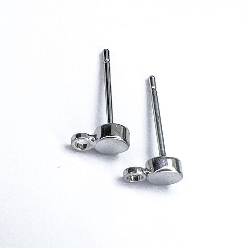 K&ouml;nnte beinhalten: Ein Paar silberne Ohrstecker mit einem kleinen Kreis-Anh&auml;nger, der an jedem Ohrstecker h&auml;ngt. Die Ohrringe haben ein schlichtes, minimalistisches Design.