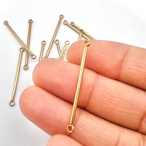 May include: A collection of gold-colored, straight bar connectors with small loops at each end. These jewelry-making components are displayed against a white background. The connectors vary in length, with the longest being approximately 1.5 inches.