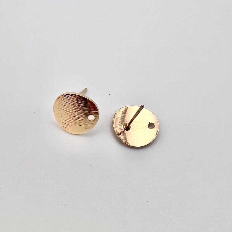 May include: Two gold-toned round earring blanks with a small hole in the center. The blanks are designed for attaching earrings.