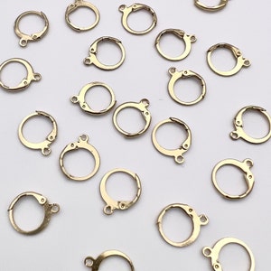 May include: A collection of gold-toned earring clasps, also known as earring findings, are scattered on a white surface. These clasps are used to attach earrings to ear wires or posts.