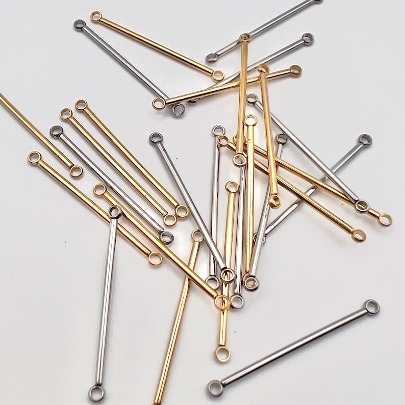May include: A collection of gold and silver-colored metal bar connectors with small loops at each end. These jewelry-making components are scattered on a white surface, showcasing their varying lengths and metallic finishes.