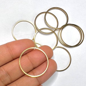 May include: A set of eight gold-coloured metal rings, some are stacked on top of each other, and some are spread out on a white surface.