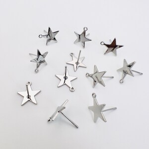 May include: A collection of silver-colored star-shaped stud earrings. Each earring features a five-pointed star design with a post and a small loop for attachment. The earrings are displayed against a white background.