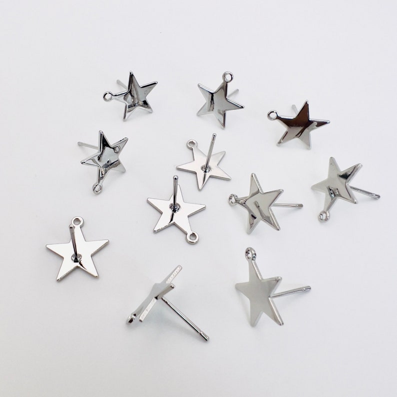 May include: A collection of silver-colored star-shaped stud earrings. Each earring features a five-pointed star design with a post and a small loop for attachment. The earrings are displayed against a white background.