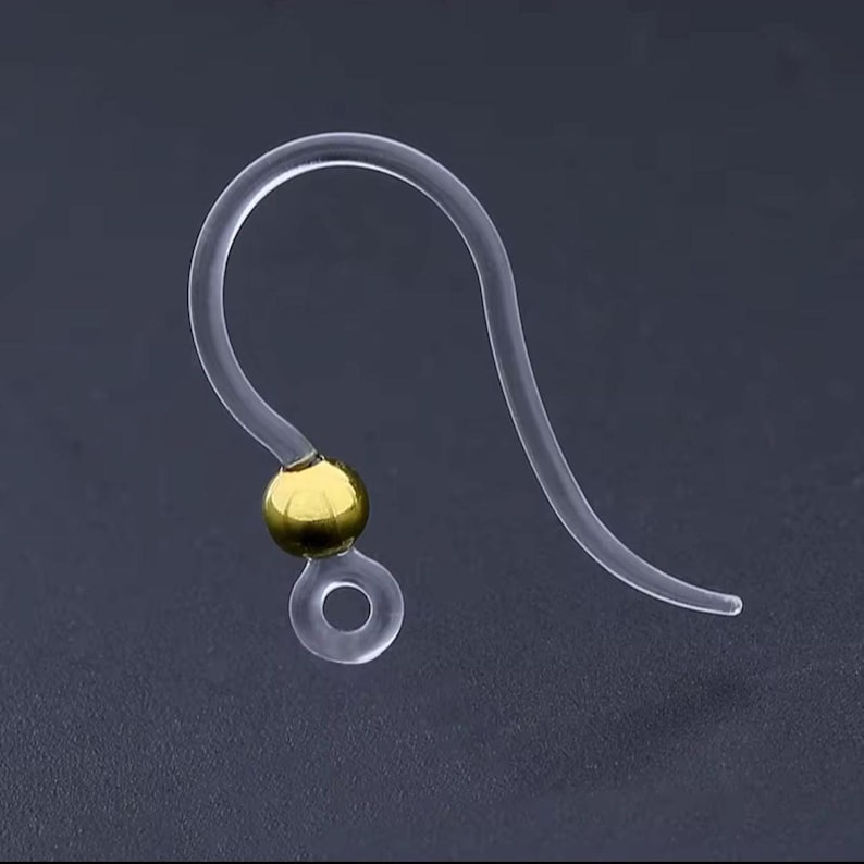 May include: Clear plastic earring hook with a gold-colored bead. The hook has a curved design with a small loop at the bottom. The earring hook is designed to be lightweight and comfortable for extended wear.