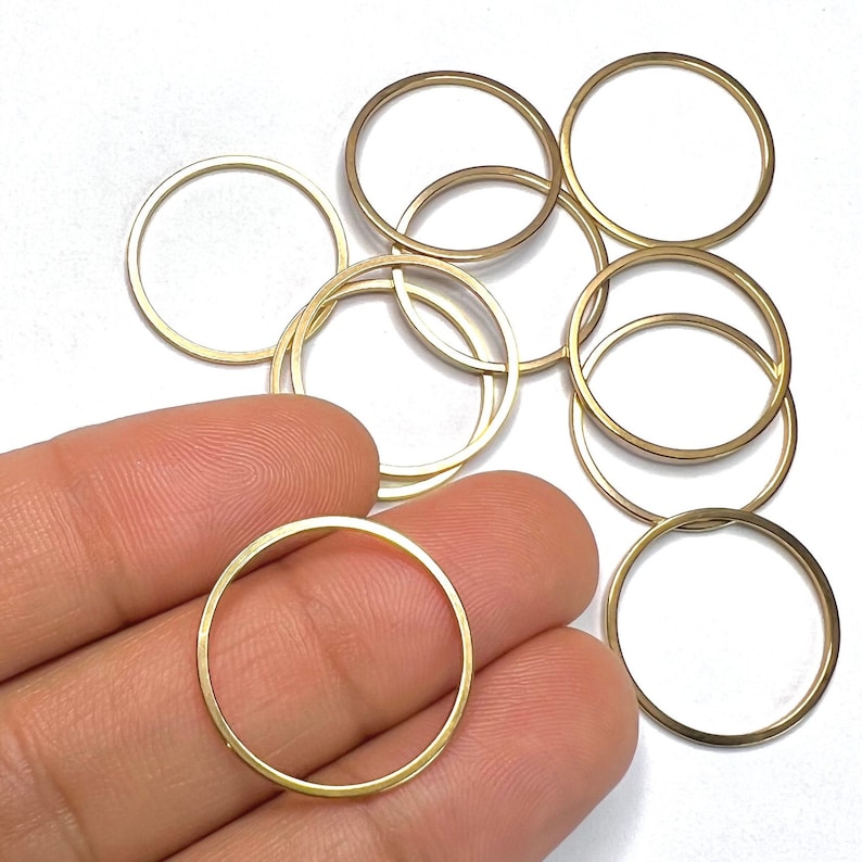 May include: A group of eight gold-coloured metal jump rings. The rings are all the same size and are arranged in a pile.