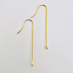 Op de afbeelding: Twee gouden oorhaken. De haken zijn lang en recht met een kleine lus aan de bovenkant.
