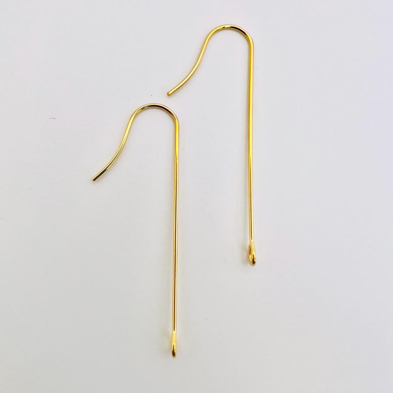 Op de afbeelding: Twee gouden oorhaken. De haken zijn lang en recht met een kleine lus aan de bovenkant.