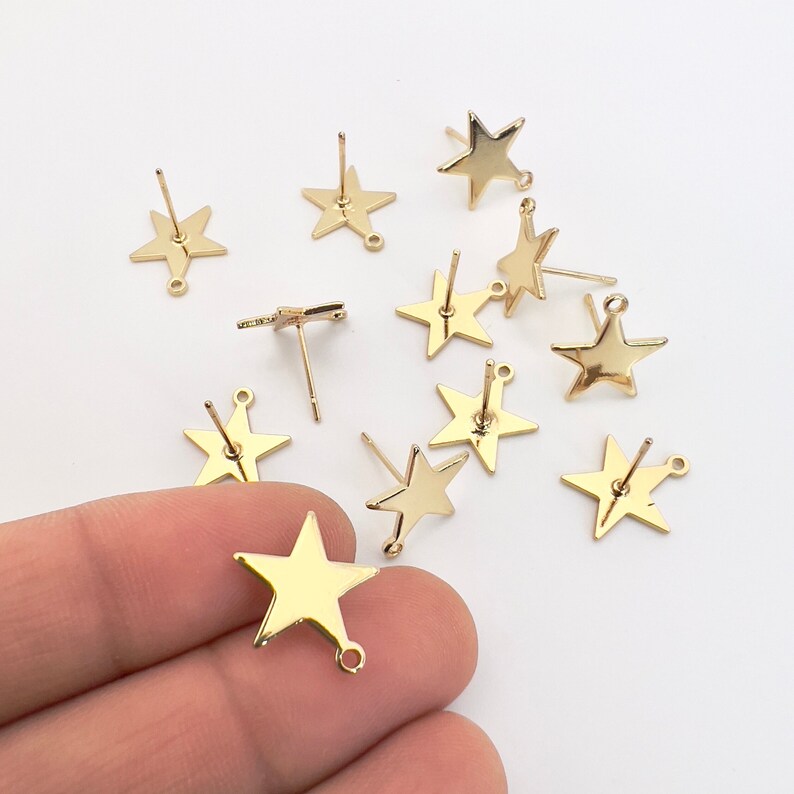 May include: Gold-colored star-shaped earring posts with a post and loop design. The earrings are shiny and have a smooth surface. The image shows several individual earring components, ideal for jewelry making or crafting.