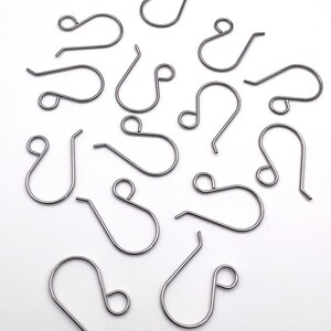 May include: A group of silver-toned earring hooks, scattered on a white surface. The hooks are all the same size and shape, with a small loop at the top and a larger loop at the bottom.