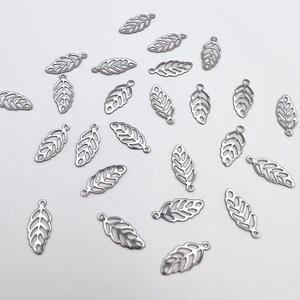May include: A collection of silver metal leaf charms with a delicate, intricate design. The charms have a hole at the top for attaching to jewelry or other crafts.