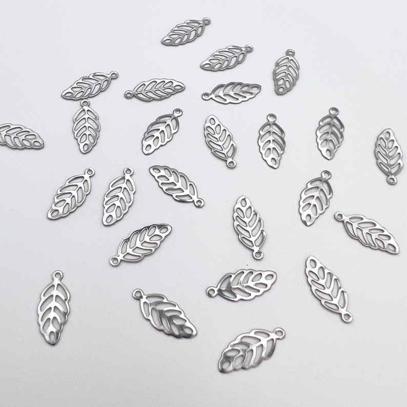 May include: A collection of silver metal leaf charms with a delicate, intricate design. The charms have a hole at the top for attaching to jewelry or other crafts.