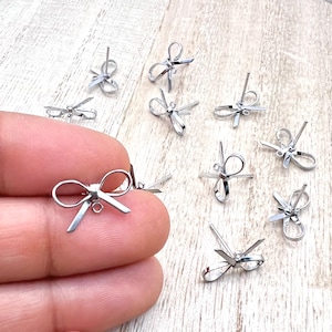May include: A group of silver bow-shaped earring findings. The findings are small and delicate, with a loop at the bottom for attaching a dangle or bead.