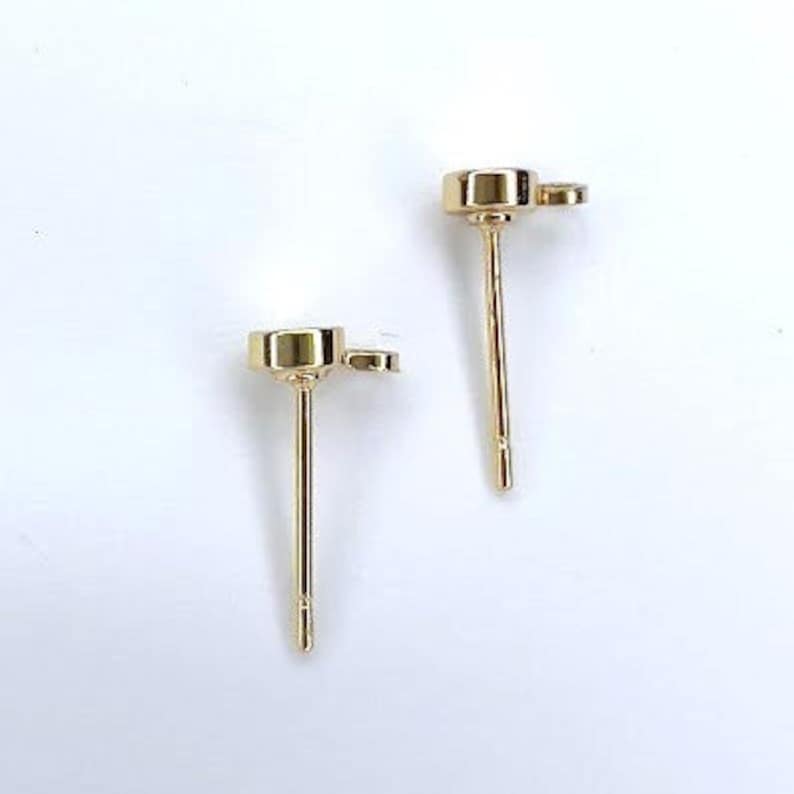 K&ouml;nnte beinhalten: Ein Paar goldene Ohrstecker mit einem kleinen runden Stein in der Mitte jedes Ohrsteckers.