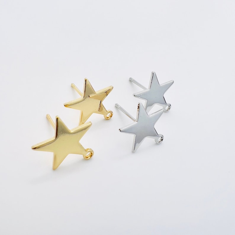 May include: Four star-shaped stud earrings. Two are gold-colored, and two are silver-colored. Each earring has a post for piercing and a small loop at the bottom. The earrings are displayed on a white surface.
