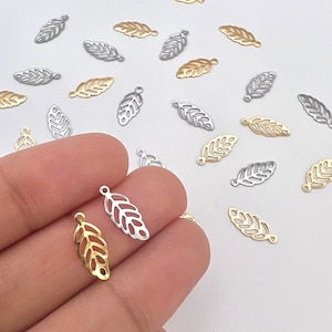 May include: A collection of gold and silver leaf-shaped charms with a hole at the top for attaching to jewelry or other crafts.