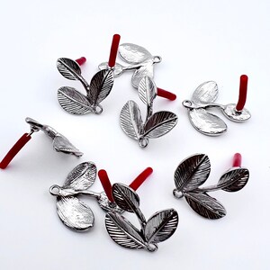 May include: Silver leaf charms with red stems. The charms are shaped like three leaves connected to a stem. The charms are perfect for jewelry making or crafting.