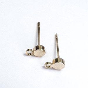 K&ouml;nnte beinhalten: Ein Paar goldfarbene Ohrstecker mit einem kleinen runden Anh&auml;nger an jedem Stecker.