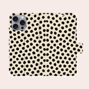Könnte beinhalten: Eine cremefarbene Handyhülle mit einem schwarzen Polka-Dot-Muster. Die Hülle im Folio-Stil hat einen Magnetverschluss. Die Handyhülle hat einen weißen Rand und einen Kameraausschnitt.