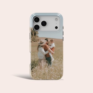 May include: A light blue phone case displaying a family portrait in a field of wildflowers. The image shows a couple holding a child. The case has a protective bumper and a glossy finish.